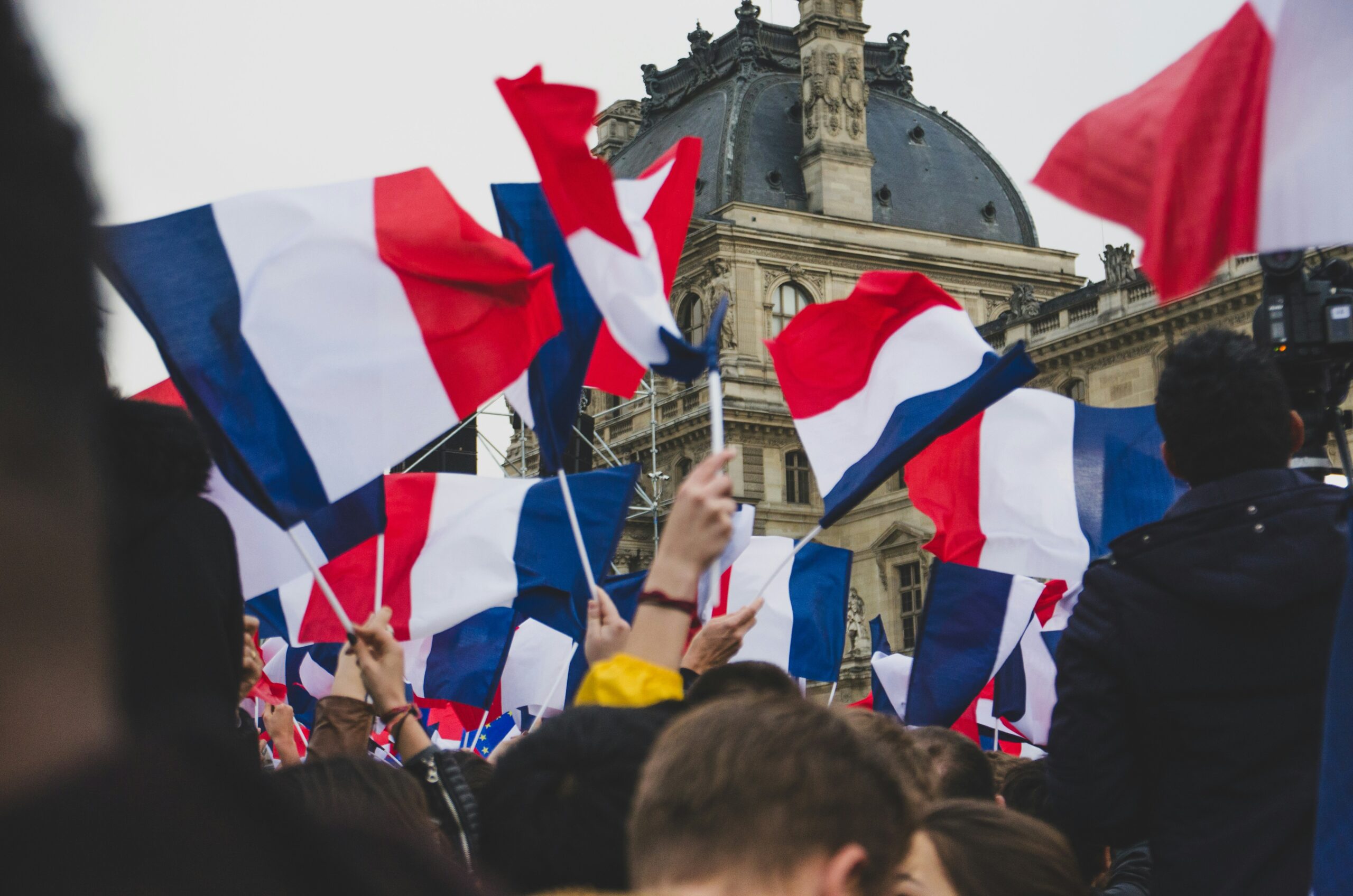 People carry a large French tricolour through a bright city street during a public demonstration
