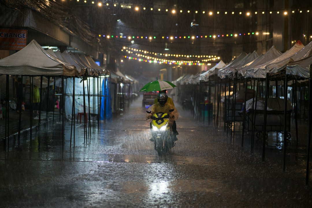 Daytime monsoon rain falls across a Bangkok street, representing the flood emergency affecting Thailand and wider Asia.