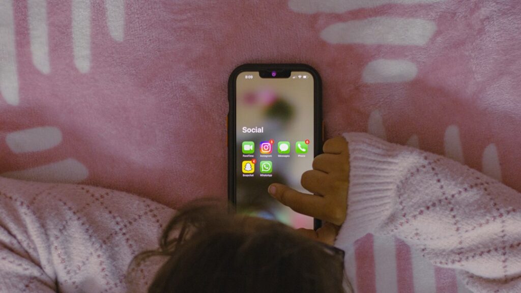 Young person using a smartphone, illustrating the debate over social media access and child online safety. Photo by Sanket Mishra on Unsplash.