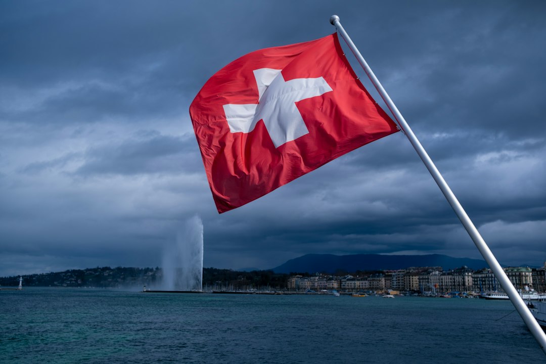 Swiss flag flying beside Lake Geneva with the Jet d’Eau in the background, illustrating Switzerland’s neutrality referendum