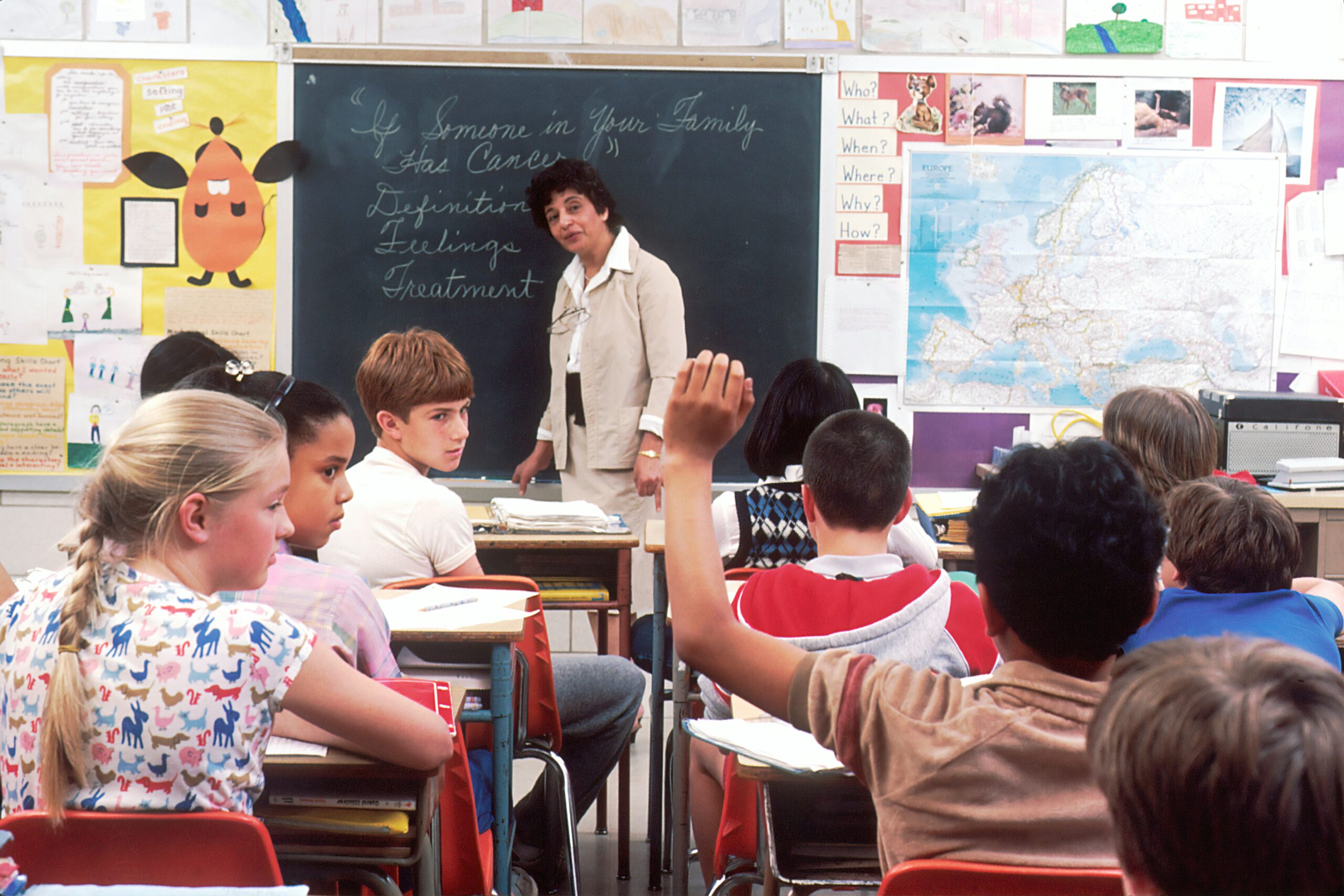 A teacher speaks with a diverse group of students seated in a bright classroom